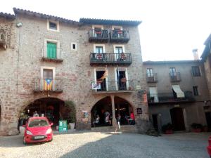 a red car parked in front of a building at CAN MENCIÓ - Plaça Major in Santa Pau