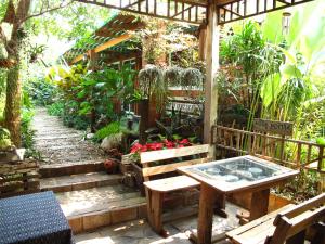 a patio with a table and benches in a garden at P.Y. Guest House in Kanchanaburi