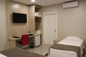 a hotel room with two beds and a desk and a television at Holiday & Business Hotel - Em frente ao Centro de Eventos e Arena Conda in Chapecó