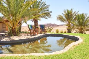 una piscina en medio de un patio con 2 sillas y palmeras en Apollis Cottage, en Springbok