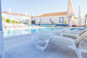 a swimming pool with white chairs and umbrellas at Monte da Ameixa Country House in Castro Verde