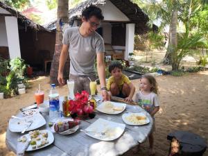 um homem e duas crianças sentados numa mesa com comida em Star Rest Surf Camp Arugambay em Arugam Bay