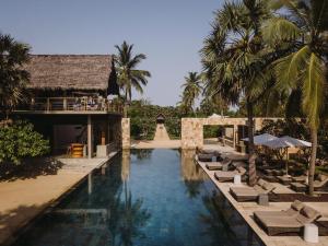 a pool at a resort with lounge chairs and palm trees at Karpaha Sands in Pasikuda