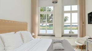 a bedroom with a white bed with two windows at Het Raadhuys - design B&B in Kessel