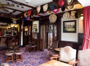 a room with a bar with a bunch of hats on the wall at The Kings Arms in Wilmslow