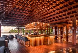 a restaurant with a bar with chairs and a wooden ceiling at JOALI Maldives in Raa Atoll