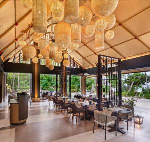 a dining room with tables and chairs and chandeliers at JOALI Maldives in Raa Atoll