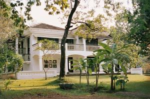 une maison blanche avec des arbres devant elle dans l'établissement The Postcard Velha, Goa, à Vieux-Goa