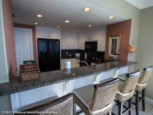 a kitchen with a counter with chairs and a black refrigerator at Treasure Island 1601 in Panama City Beach