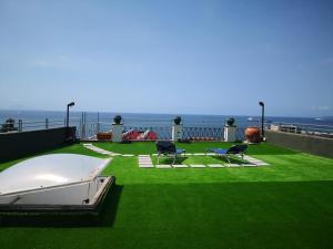 um quintal com relva verde e cadeiras e o oceano em Attico Blu em Nápoles
