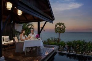 a man and woman sitting at a table with the ocean in the background at Anantara Lawana Koh Samui Resort in Chaweng