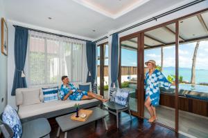 two people sitting in a living room with windows at NH Collection Samui Peace Resort in Bophut