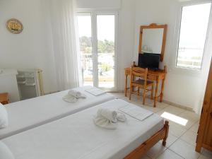 a white bedroom with two beds and a mirror at Hotel Sgouridis in Limenaria