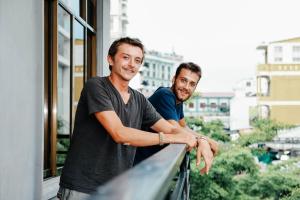 two men standing on a balcony looking out of a window at DMZ Hostel in Hue