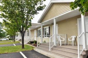 a house with white chairs on the front porch at Motel Blanche d'Haberville in Saint-Jean-Port-Joli