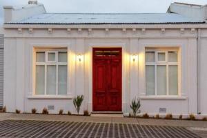 a white building with a red door and two windows at Hostal Boutique Puerta Roja in Punta Arenas