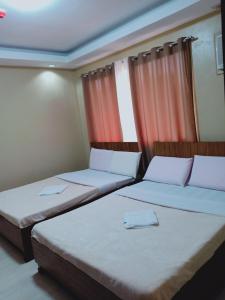 two beds in a room with orange curtains at East Square Inn in Bacolod