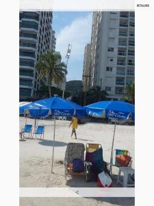 a person walking on a beach with blue umbrellas and chairs at Apartamento Vista Mar - 2 Garagens in Guarujá