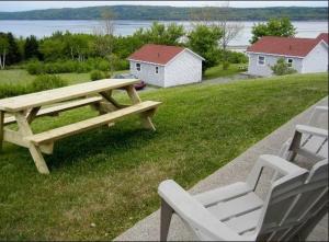 una mesa de picnic de madera y 2 sillas en un campo en Chisholms of Troy Coastal Cottages, en Port Hawkesbury