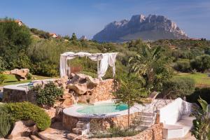 a pool in a garden with a mountain in the background at Hotel Ollastu in Costa Corallina