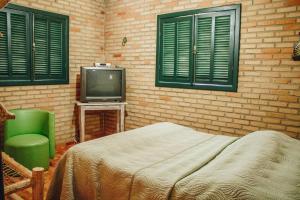 um quarto com uma cama, uma televisão e uma parede de tijolos em Verdes Em Cantos Pousada em Carrancas