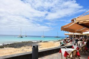 - une plage avec des tables, des chaises et des bateaux dans l'eau dans l'établissement VIP HOLIDAYS Morro Jable Beach & Center 1, à Morro del Jable