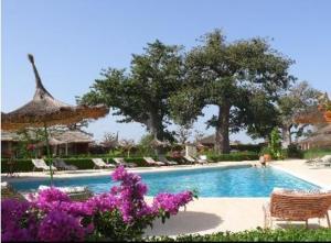 a swimming pool with chairs and trees and purple flowers at Baobab Soleil in Sindia