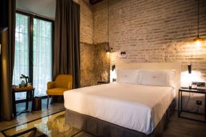 - une chambre avec un lit blanc et un mur en briques dans l'établissement Hotel Legado Alcazar, à Séville