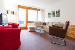 sala de estar con sofá blanco y sillas rojas en Residenz Alpina 115 en Lenzerheide
