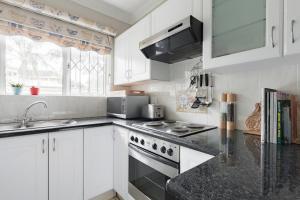 Banana palm luxury cottage في ديربان: مطبخ مع خزائن بيضاء وقمم منضدة سوداء