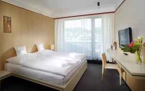 Cette chambre comprend un lit, un bureau et une fenêtre. dans l'établissement Alexandria Spa & Wellness Hotel, à Luhačovice