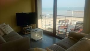 een woonkamer met 2 banken, een televisie en een balkon bij Studio apartment 'De Strandwandeling' with frontal sea view near Ostend in Oostende