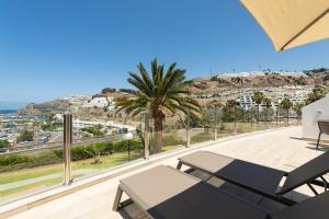 a balcony with a view of a city and a palm tree at Holiday Club Puerto Calma in Puerto Rico de Gran Canaria