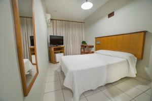 a bedroom with a white bed and a television at Hotel Leiria in Matão