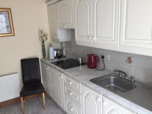 a kitchen with white cabinets and a sink and a chair at Tafelta Lodge in Magherafelt
