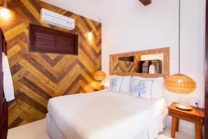 1 dormitorio con cama blanca y pared de madera en Pousada Jequitibá, en Trancoso