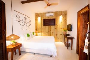 1 dormitorio con cama blanca y pared de madera en Pousada Jequitibá, en Trancoso