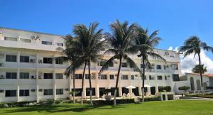 a large white building with palm trees in front of it at Apartamentos Beira Mar Marinas Tamandare PRAIA DOS CARNEIROS in Praia dos Carneiros