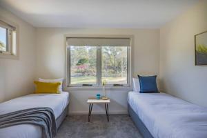 two beds in a room with a window at Baileys Beach House in Binalong Bay