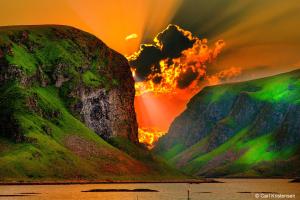 a sunset over a mountain with a green eruption at Røst Bryggehotell in Røst