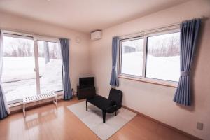 ein Wohnzimmer mit einem Sessel und zwei Fenstern in der Unterkunft Trailside Apartments Niseko in Kutchan