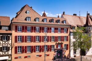 a large building with red windows in a city at Hotel Le Colombier in Colmar