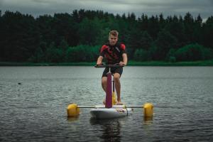 a man riding a stand up paddle board on the water at Kupiškėnų Starkėnas in Palėvenėlė