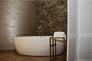 a bath tub in a bathroom with a brick wall at Hotel Ambasada in Krobia
