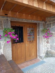 uma porta de madeira de um edifício de pedra com flores cor-de-rosa em Habitación do Xurés em Maus de Salas