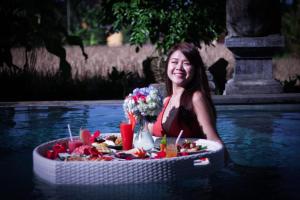 une femme assise dans l'eau avec une table de nourriture dans l'établissement Villa Heron Ubud, à Ubud