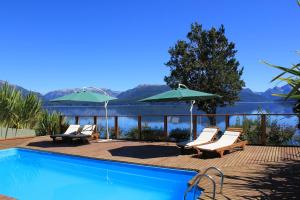 una piscina con sillas y sombrillas junto a un lago en Cabañas Quetrihue en Villa La Angostura