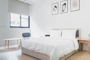 a white bedroom with a bed and a chair at Boléro Homestay in Tainan
