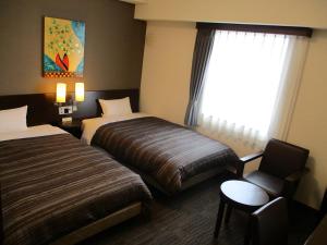 a hotel room with two beds and a chair and a window at Hotel Route-Inn Kitakyushu-Wakamatsu Ekihigashi in Kitakyushu