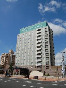 un gran edificio blanco con un letrero verde. en Hotel Route-Inn Kitakyushu-Wakamatsu Ekihigashi, en Kitakyushu